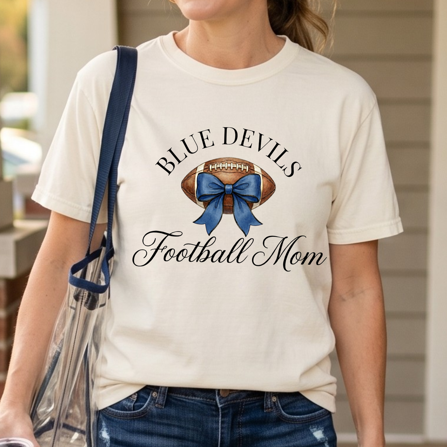 Person wearing a 'Blue Devils Football Mom' t-shirt with a football and blue bow design.