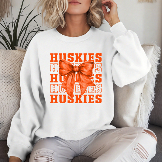 Hamilton Heights Huskies coquette bow crewneck sweatshirt featuring layered varsity typography and oversized orange bow graphic on white sweatshirt