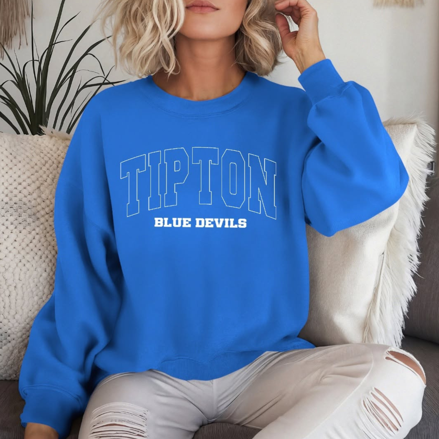 Person wearing a blue sweatshirt with 'TIPTON BLUE DEVILS' text, sitting on a couch.