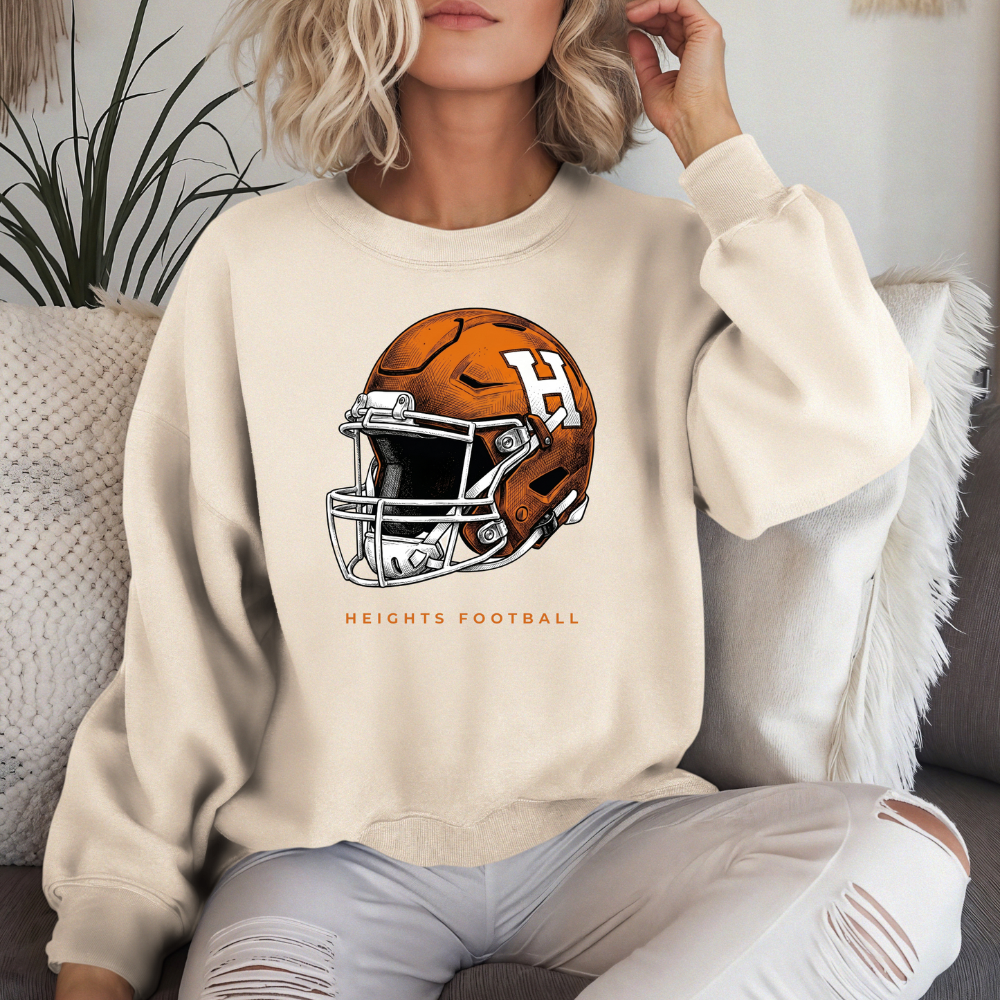 A person lounging in a cream-colored crewneck sweatshirt with an orange and white Hamilton Heights football helmet graphic.