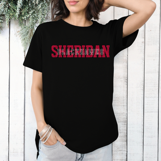Woman wearing a black t-shirt featuring a layered, vintage-style Sheridan Blackhawks typography design.