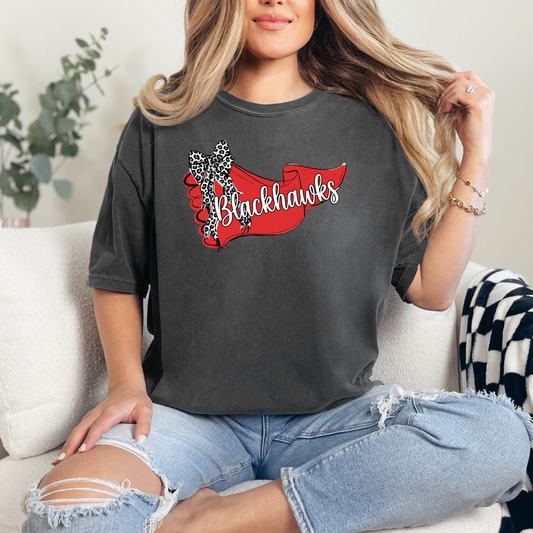 Woman wearing a charcoal graphic t-shirt featuring a Blackhawks team banner and leopard-print bow design, sitting on a couch.