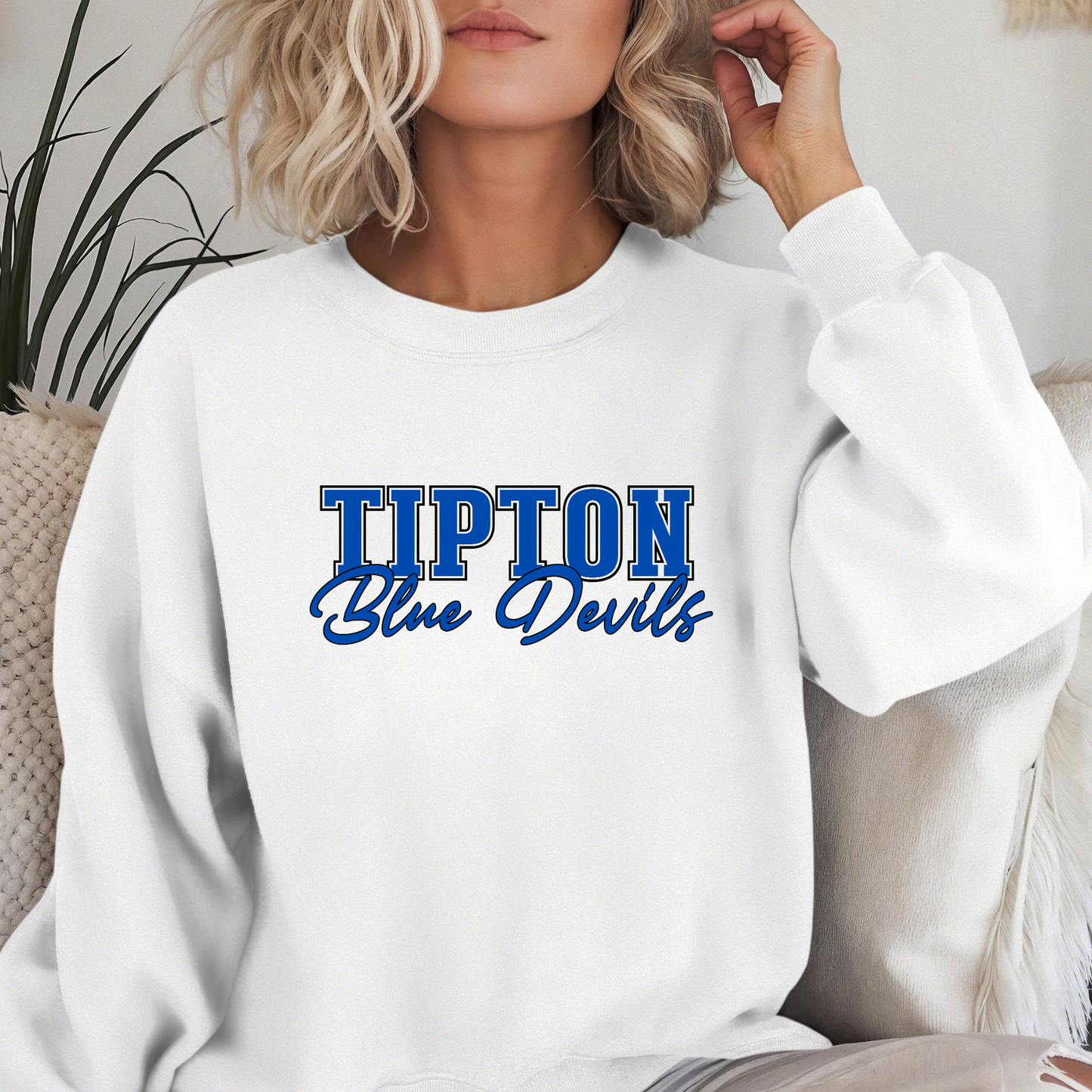 Woman wearing a white Tipton Blue Devils Script Spirit Crewneck Sweatshirt featuring bold blue varsity lettering with Blue Devils script design in royal blue, white, and black school colors.