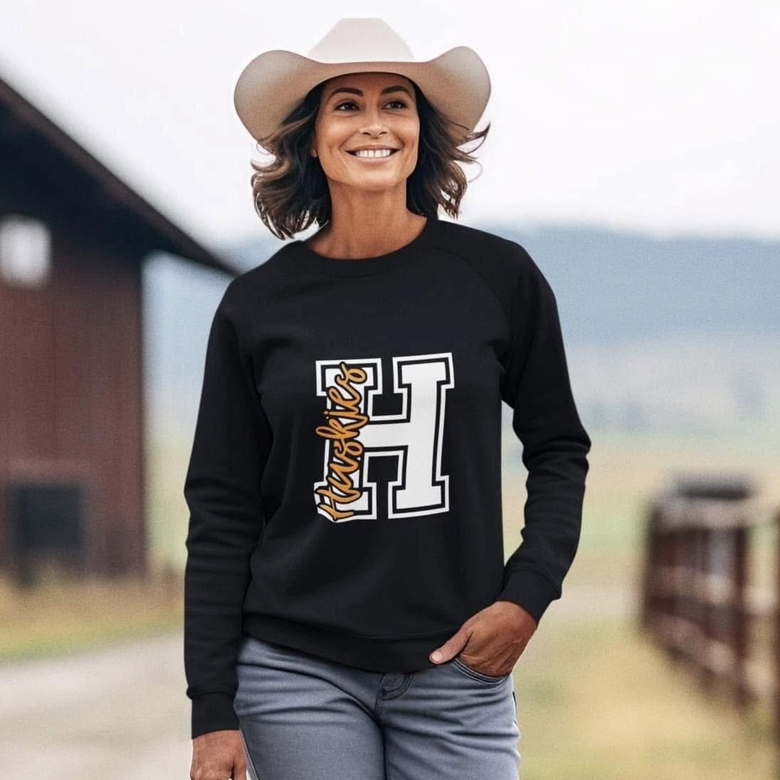 Woman wearing a Hamilton Heights Huskies H crewneck sweatshirt, black and white varsity letter design, school spirit wear.
