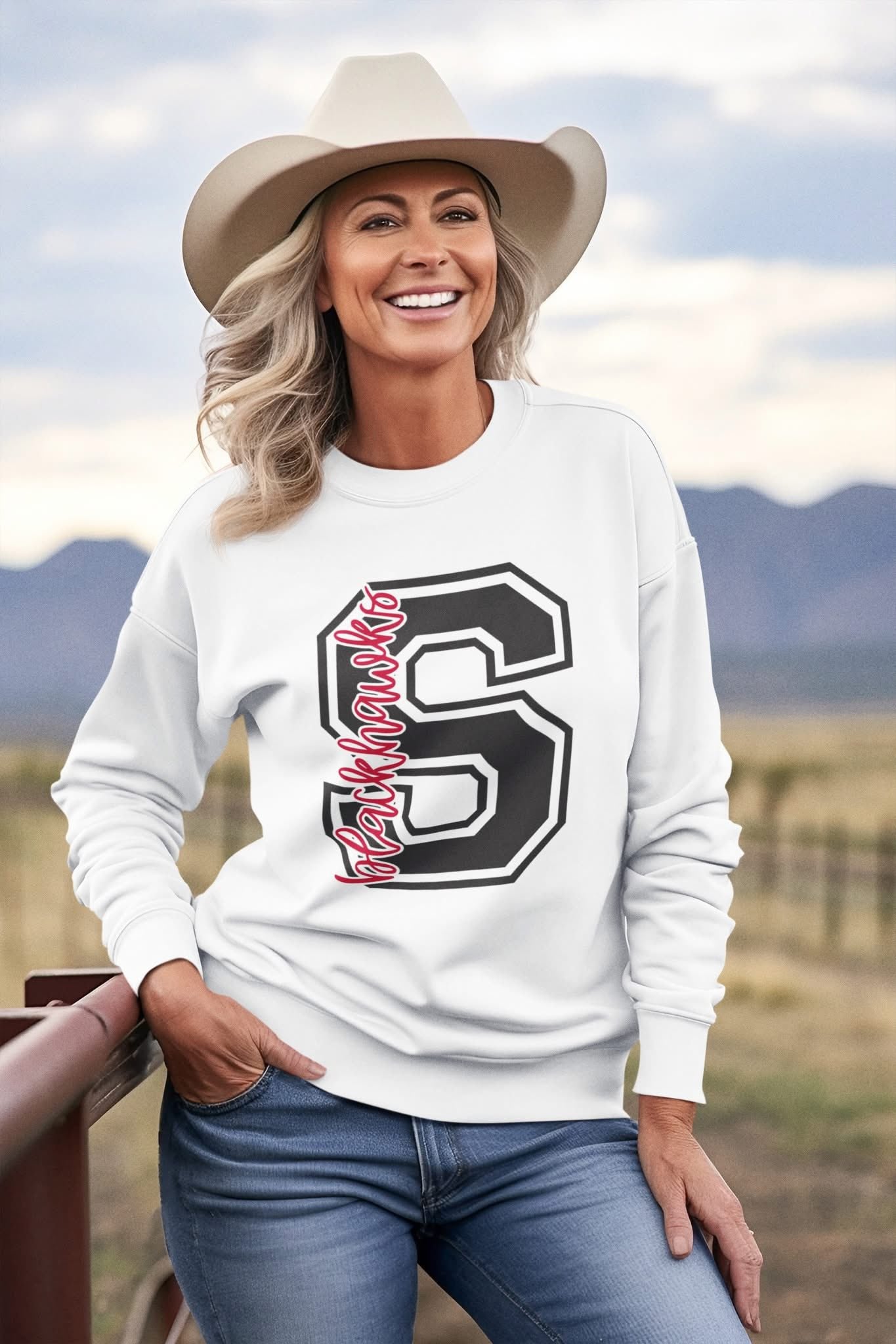 Woman wearing a white Sheridan Blackhawks varsity letter S crewneck with black detailing, standing outdoors.