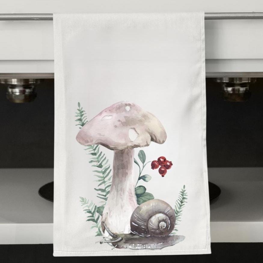 Kitchen towel with a mushroom and snail design hanging on a cabinet.