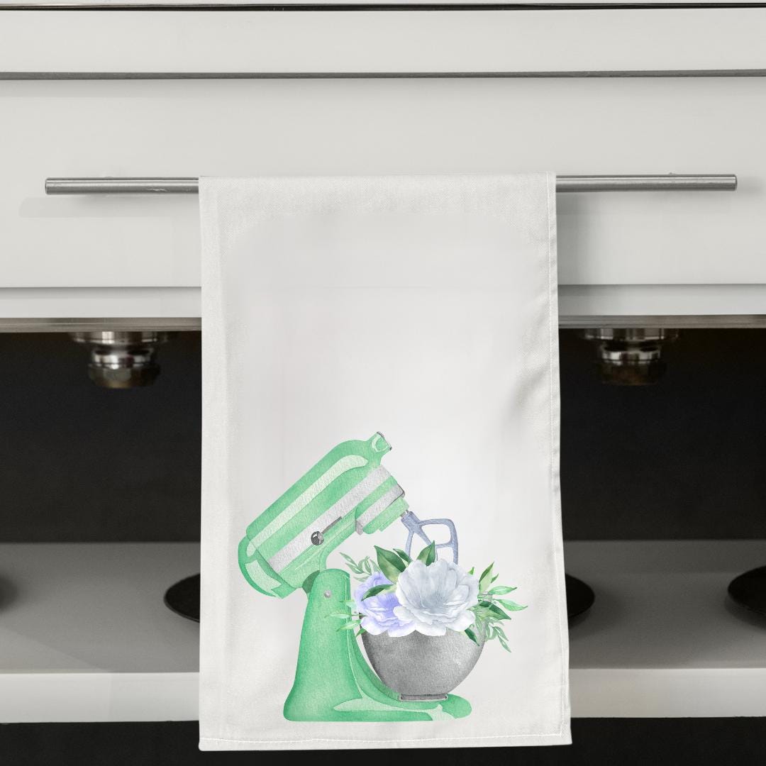 Kitchen towel with a mixer and flower design hanging on a cabinet handle.