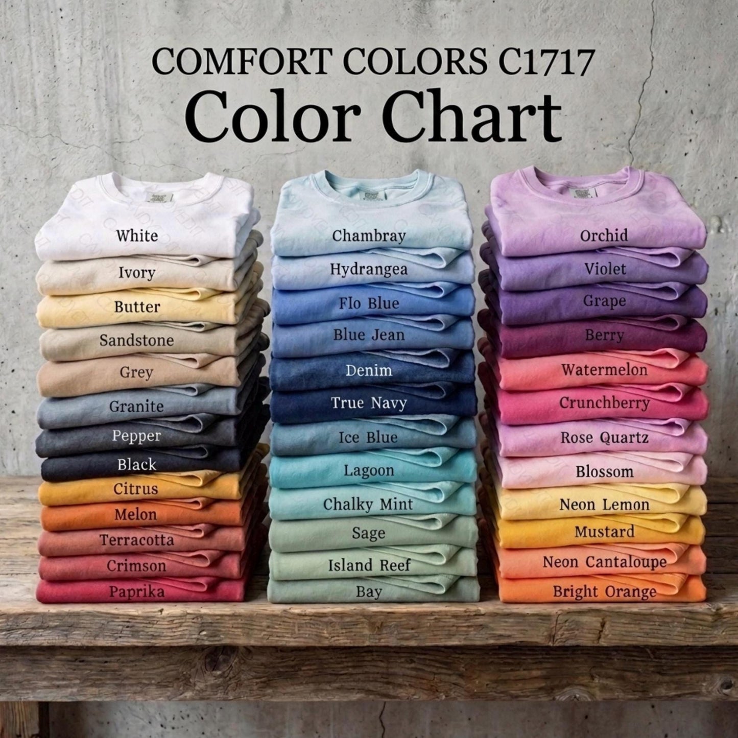 Stacks of folded shirts labeled with color names on a wooden surface against a concrete wall.