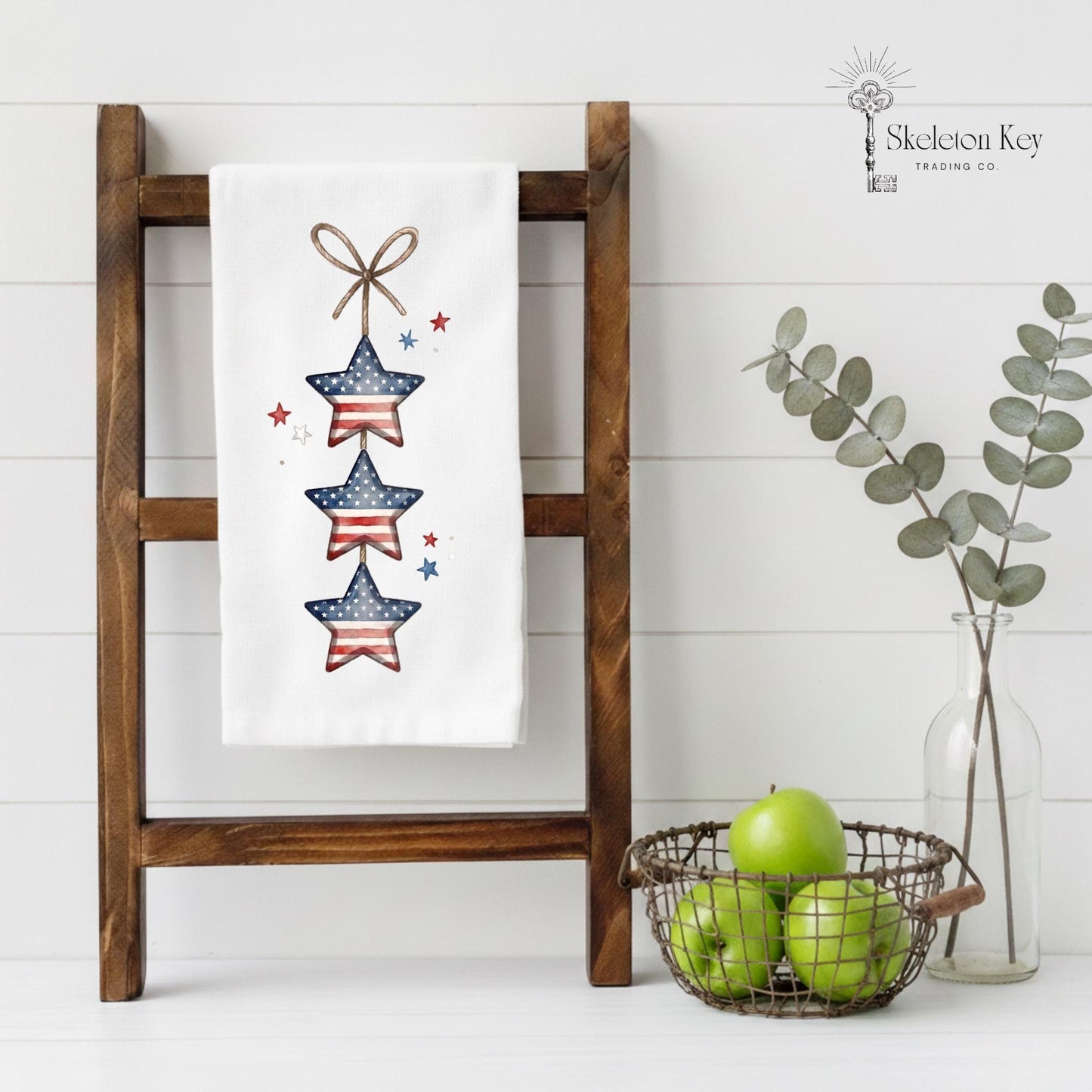 Decorative towel with star design on a wooden ladder against a white wall, with a basket of apples and a vase of eucalyptus.