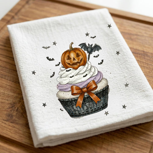 Halloween cupcake tea towel with pumpkin jack-o'-lantern decoration, purple frosting, bats, and festive fall accents