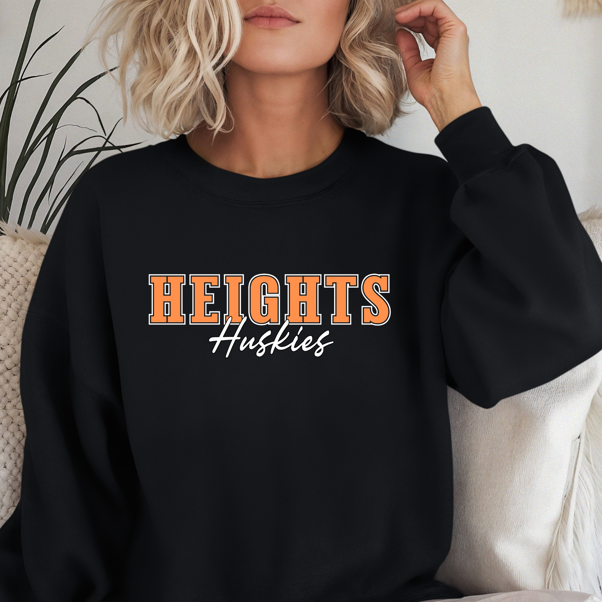 Woman wearing a black Heights Huskies Script Spirit Crewneck Sweatshirt featuring bold orange varsity lettering with Huskies script design in school colors on a comfortable crewneck sweatshirt.