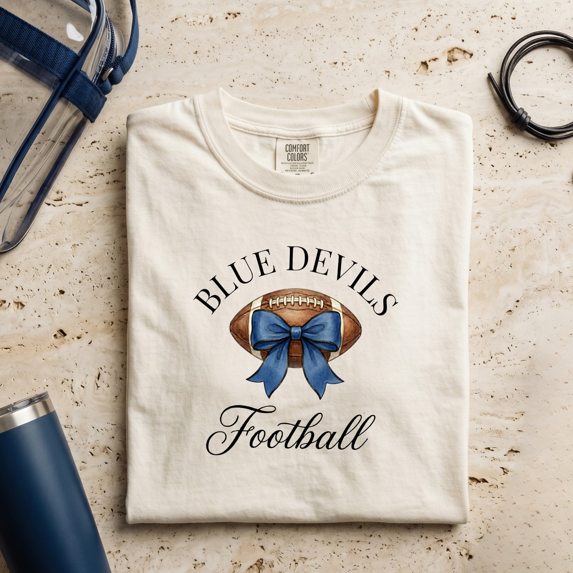 Folded t-shirt with 'Blue Devils Football' design on a textured surface with accessories.