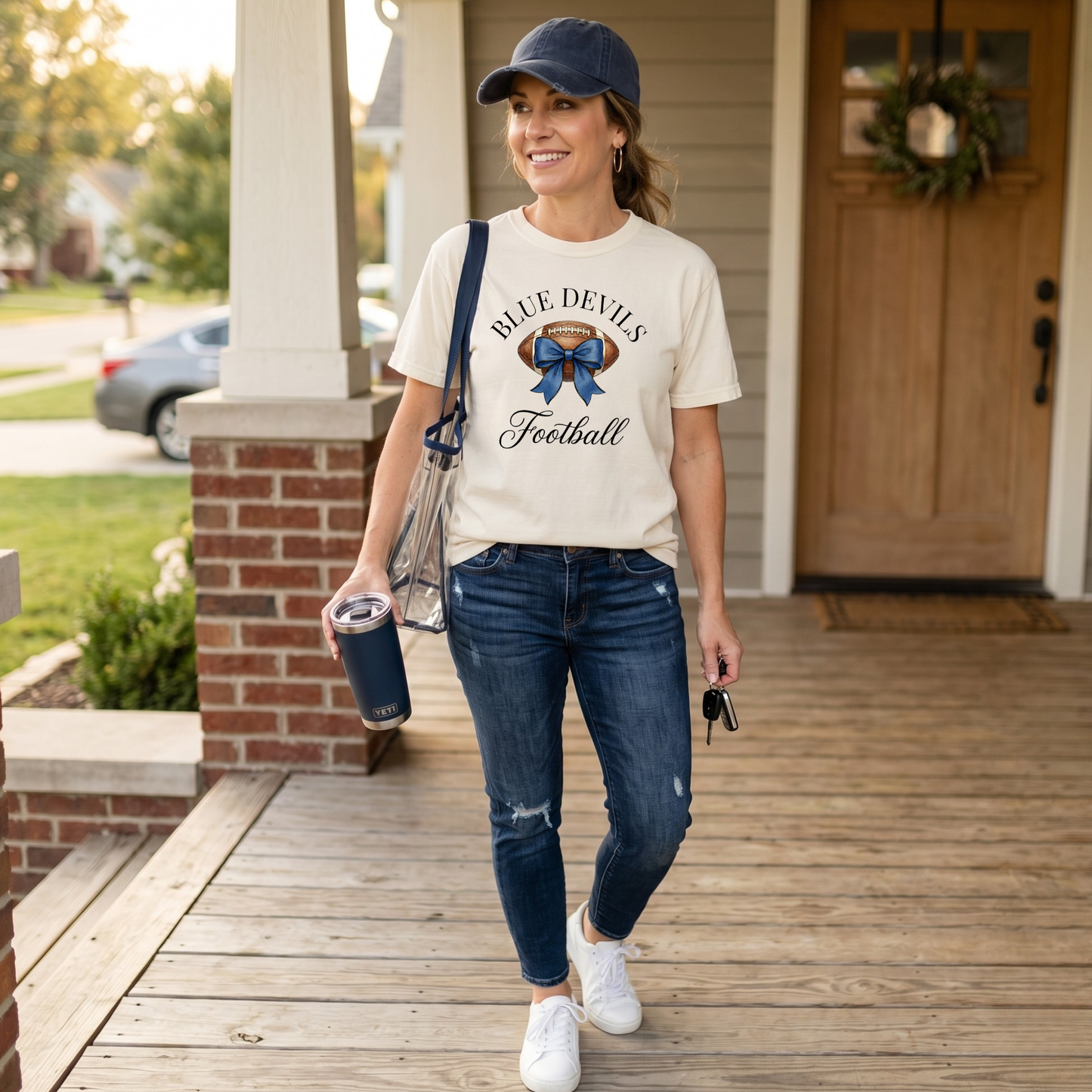 Woman walking on a porch wearing a 'Blue Devils Football' t-shirt, blue jeans, and a navy cap.