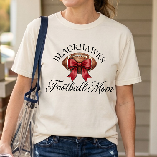 Woman wearing Sheridan Blackhawks Football Mom shirt with watercolor football and red bow design for game day spirit wear