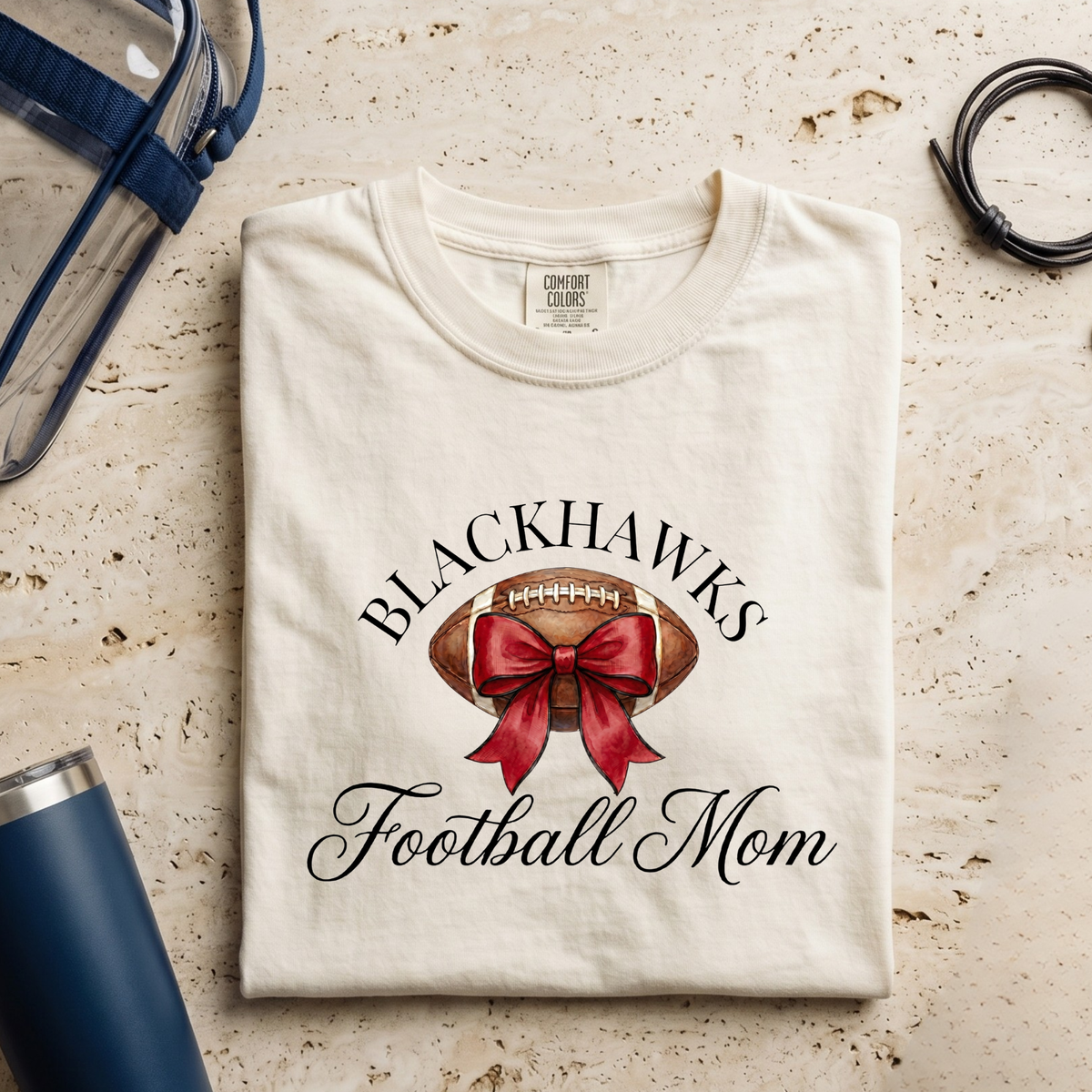 Sheridan Blackhawks Football Mom shirt featuring watercolor football and red bow design on Comfort Colors garment-dyed tee