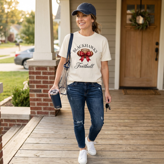 Woman wearing Sheridan Blackhawks Football shirt featuring a watercolor football with red bow graphic on a Comfort Colors tee
