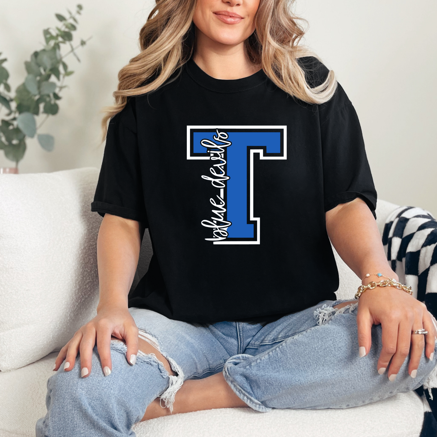 Person wearing a black t-shirt with a blue letter 'T' design, sitting on a couch.