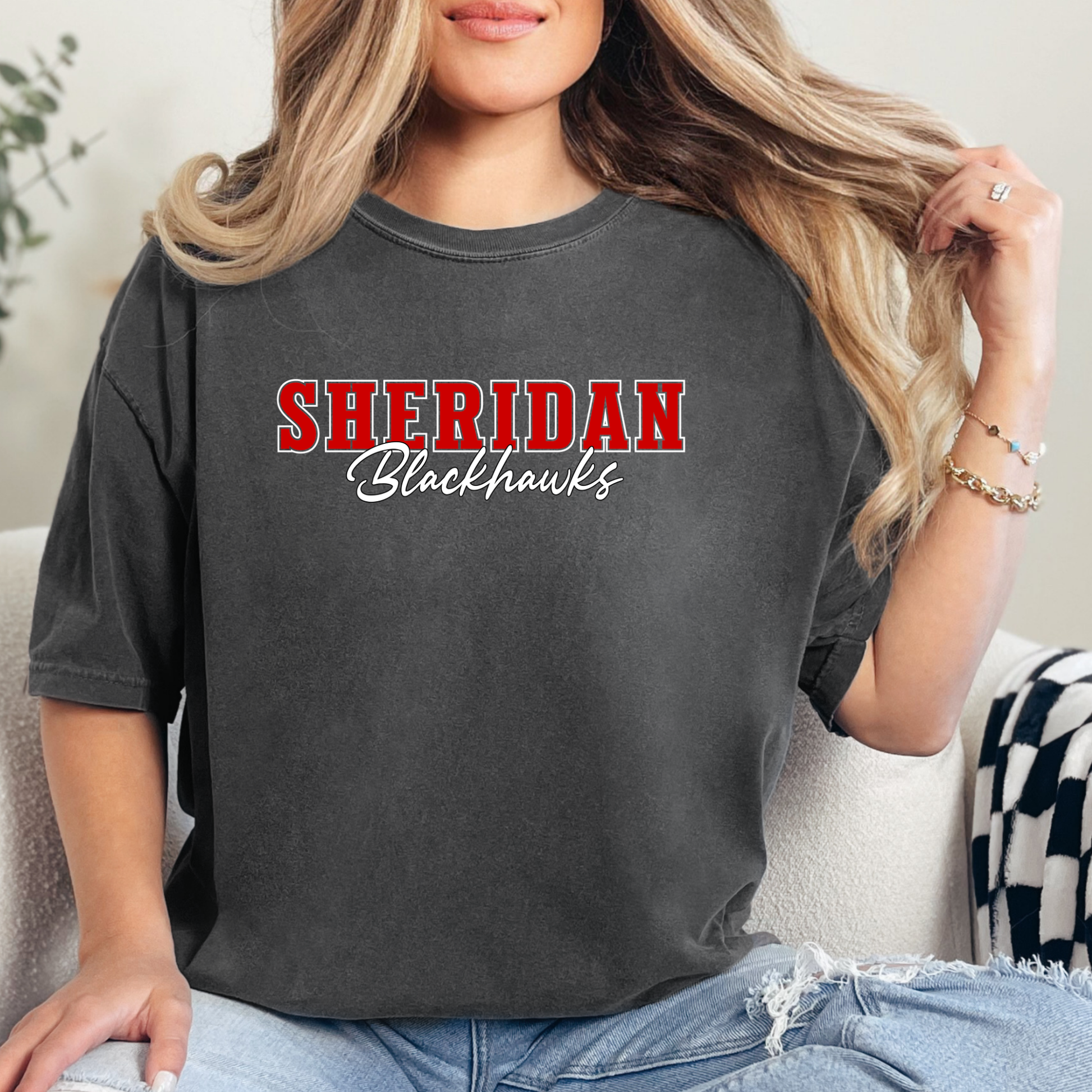 Woman wearing a pepper grey Sheridan Blackhawks Script Spirit Shirt featuring bold red varsity Sheridan lettering with Blackhawks script design on a unisex t-shirt.