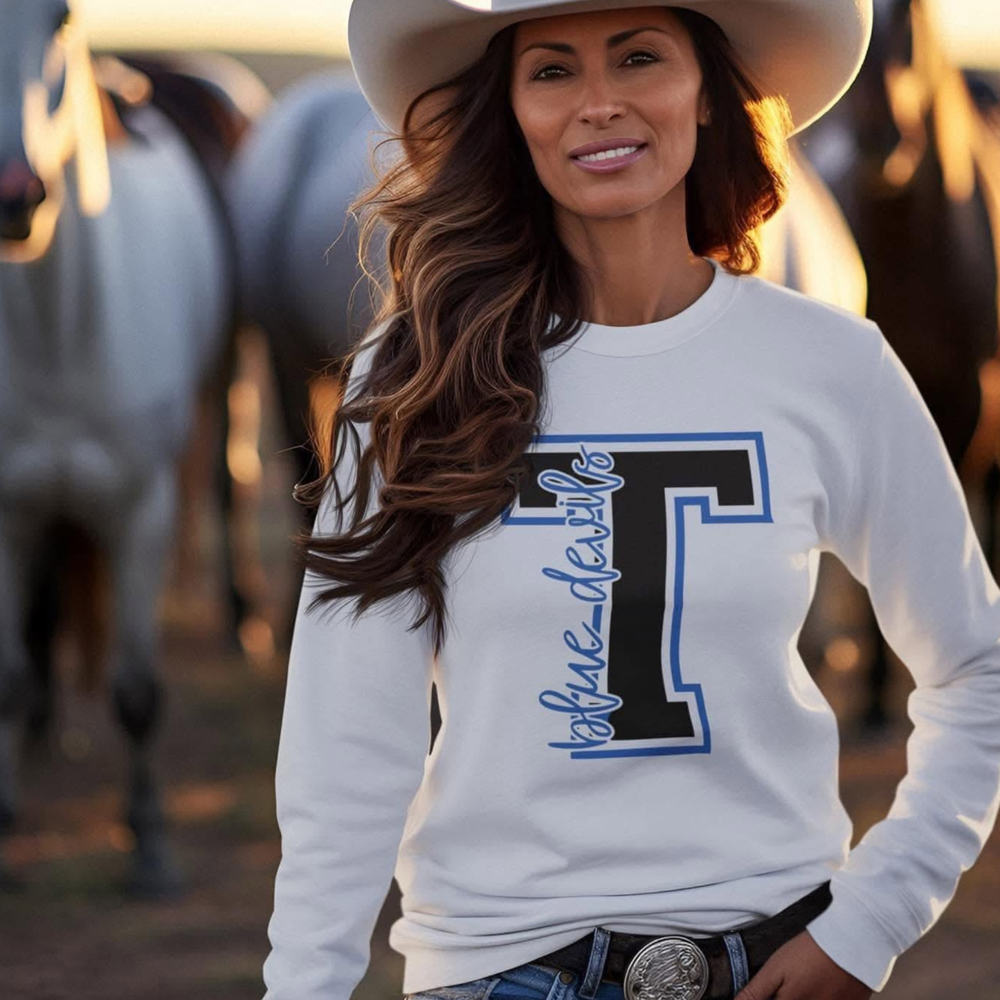 Woman wearing a white sweatshirt with a large letter 'T' and cowboy hat, standing in front of horses.