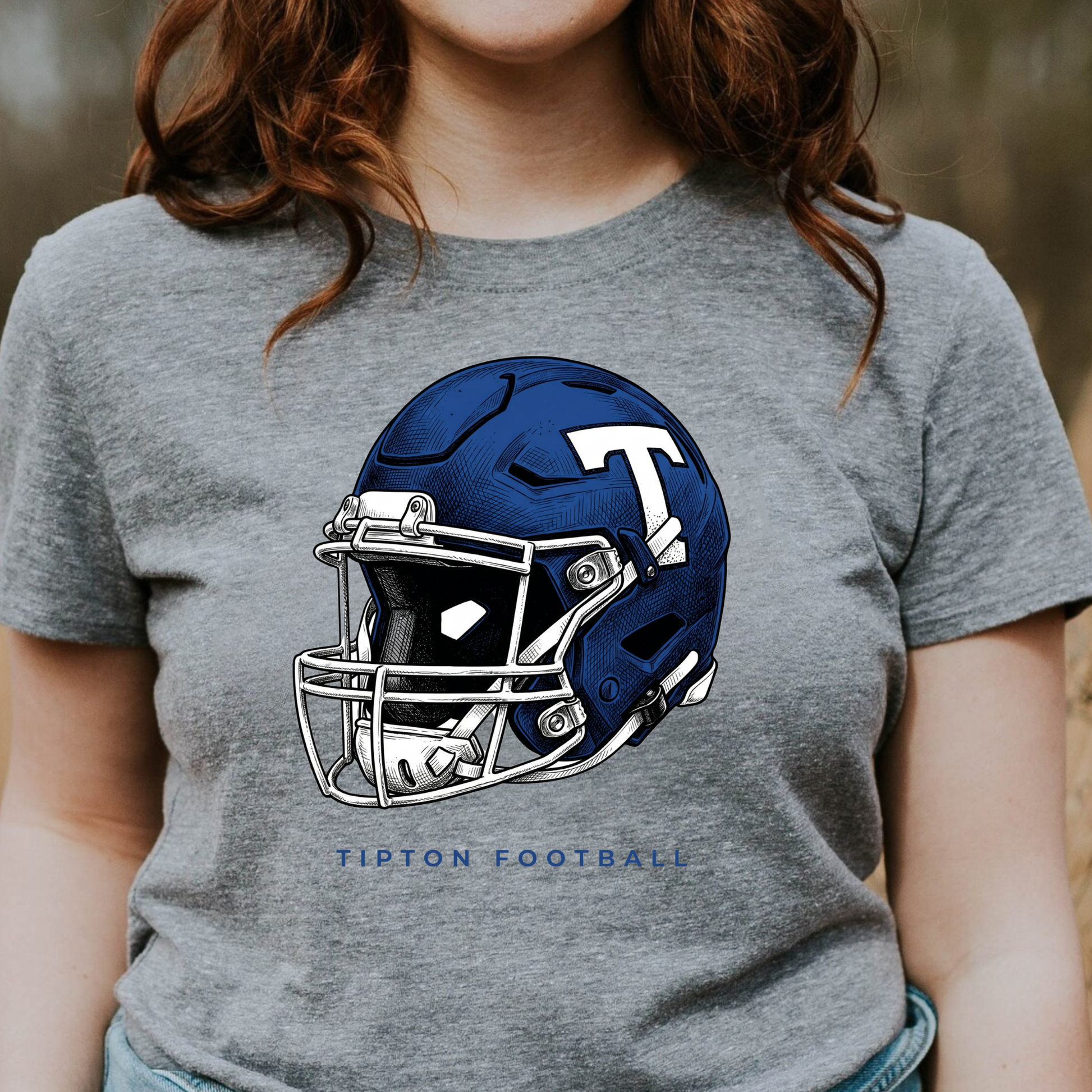 Woman wearing a grey graphic t-shirt featuring a detailed Tipton Blue Devils football helmet illustration.