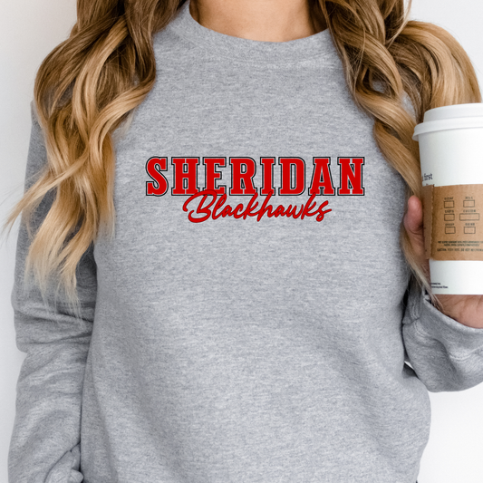 Woman wearing a grey Sheridan Blackhawks Script Spirit Shirt featuring bold red varsity Sheridan lettering with Blackhawks script design on a unisex crewneck sweatshirt.