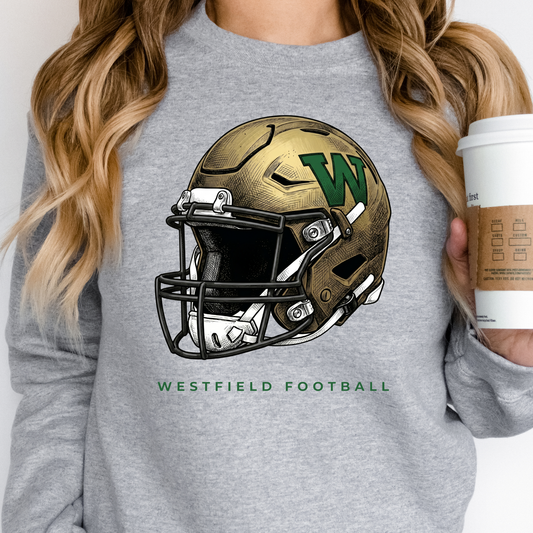 A person wearing a grey crewneck sweatshirt featuring a gold and green Westfield football helmet design with the text 'WESTFIELD FOOTBALL', holding a coffee cup.