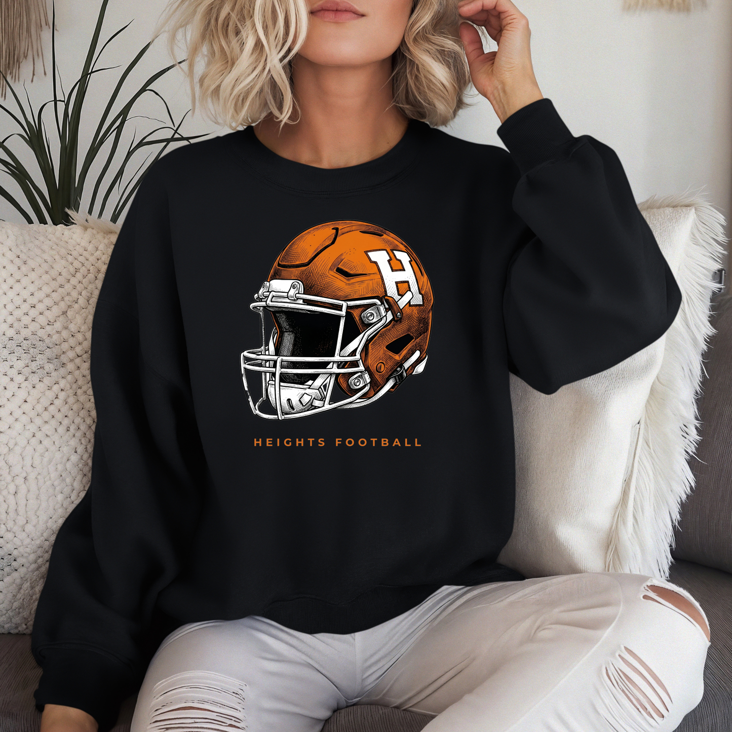 A person wearing a black crewneck sweatshirt with an orange and white Hamilton Heights football helmet design and 'HEIGHTS FOOTBALL' text.