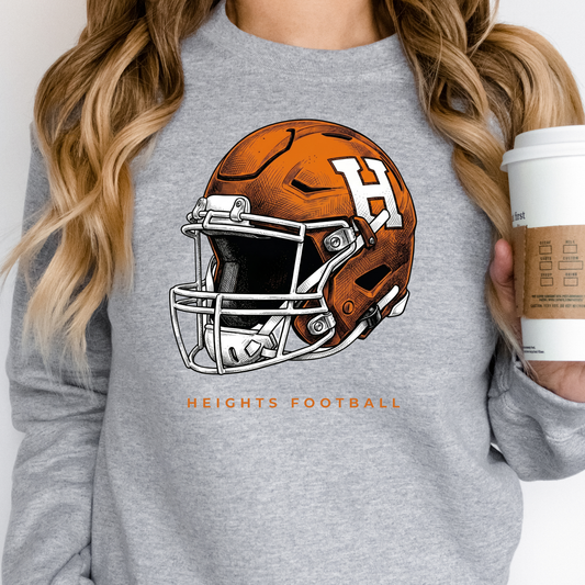 A person wearing a grey crewneck sweatshirt featuring an orange and white Hamilton Heights football helmet design, holding a coffee cup.