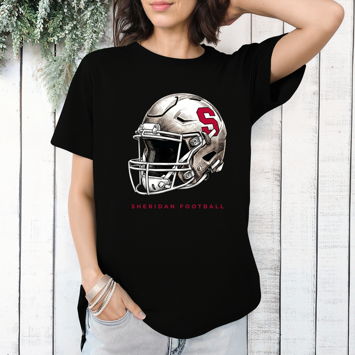 Black crewneck t-shirt featuring a modern Sheridan Blackhawks football helmet graphic and Sheridan Football text on a white wood background.