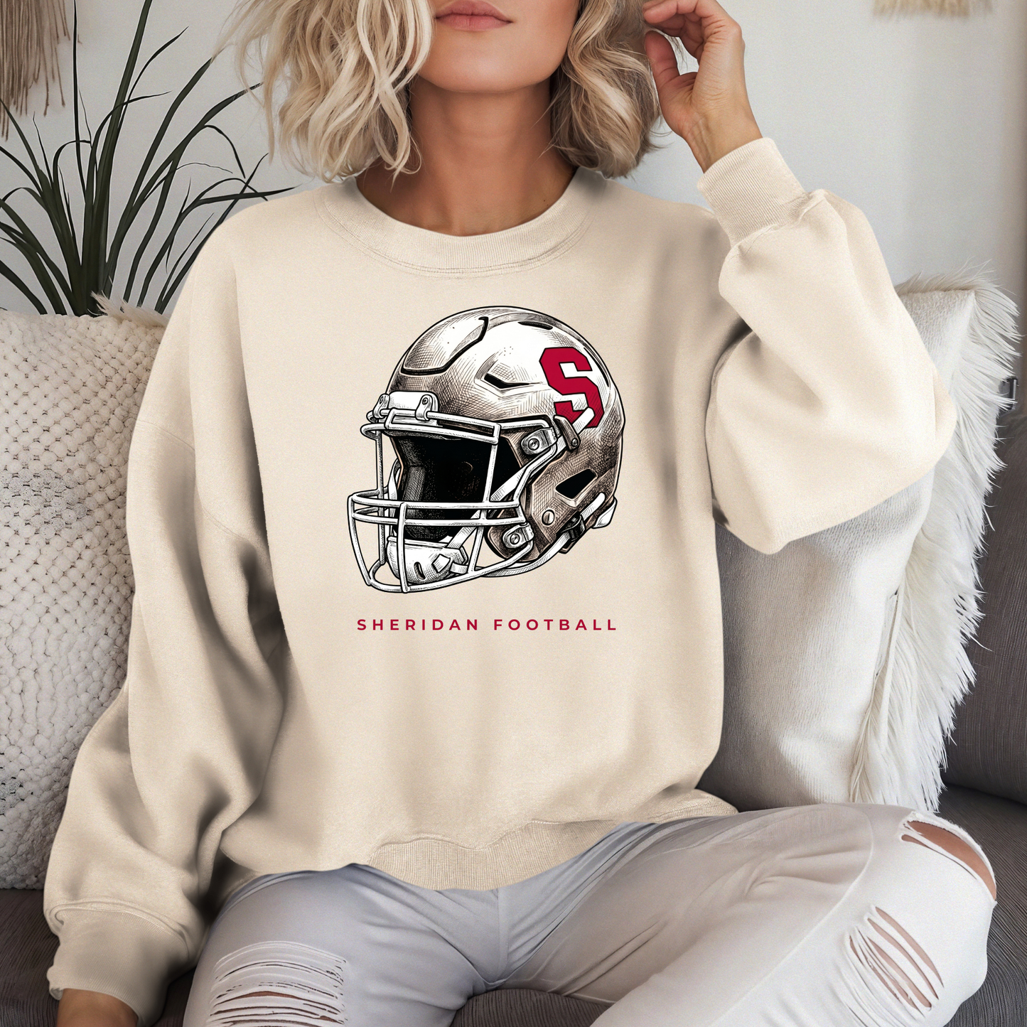 Woman in a cream-colored premium crewneck sweatshirt featuring a detailed Sheridan Blackhawks football helmet graphic.