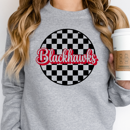 A woman wearing a Sheridan Blackhawks checkered crewneck sweatshirt featuring red script lettering over a black and gray checkerboard design 