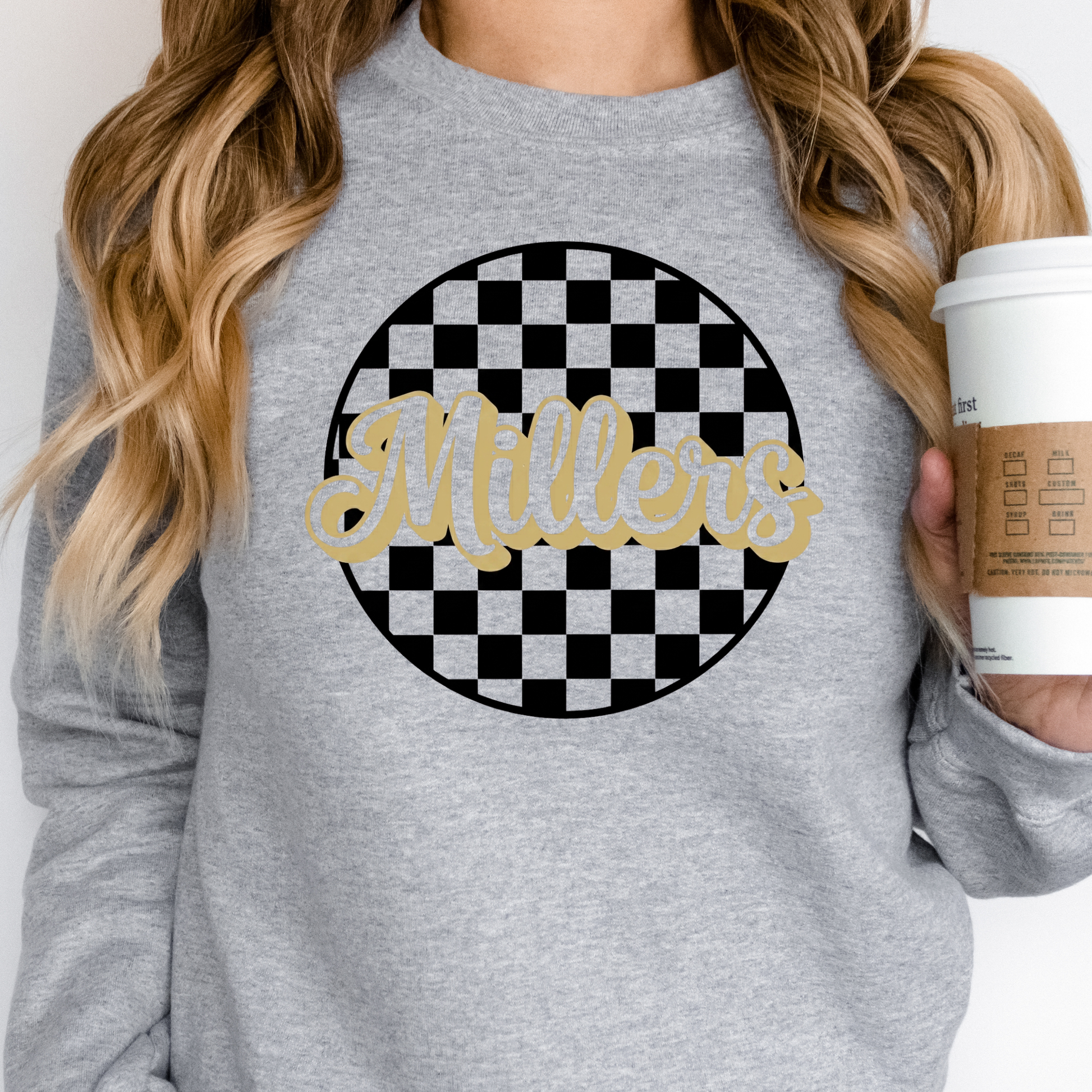 Woman wearing a gray sweatshirt with 'Millers' design, holding a coffee cup.