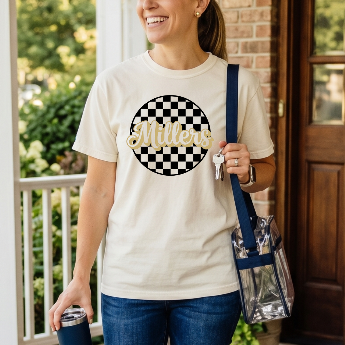 Woman wearing a white t-shirt with a checkered circle design and 'Bulldogs' text, holding a blue bag and a blue tumbler.