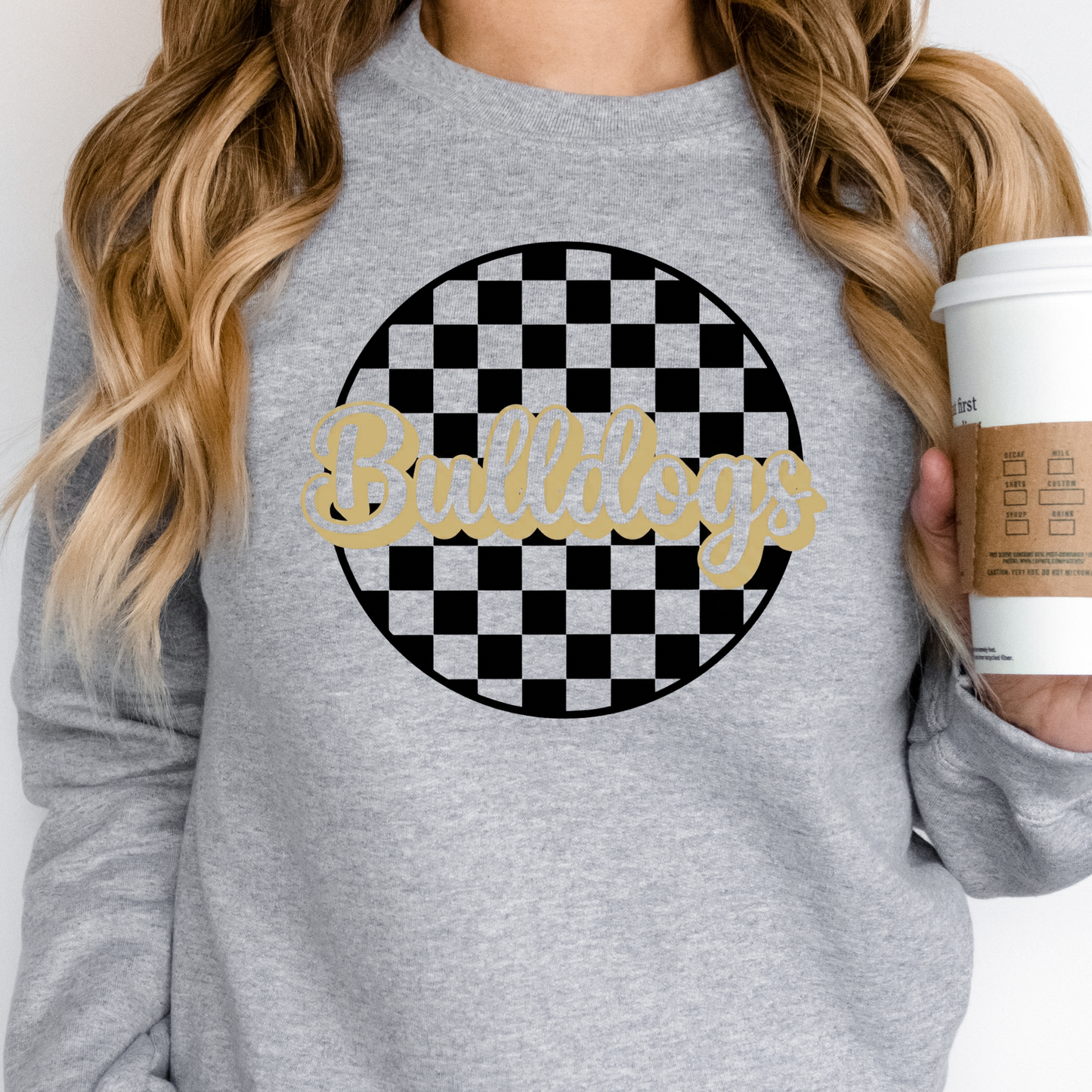 Woman  wearing a gray sweatshirt with 'Bulldogs' design and holding a coffee cup.