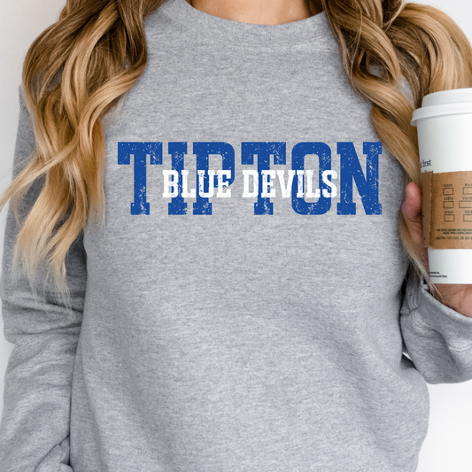 Person wearing a grey crewneck sweatshirt featuring a distressed 'TIPTON' and 'BLUE DEVILS' block-lettering design, holding a coffee cup.