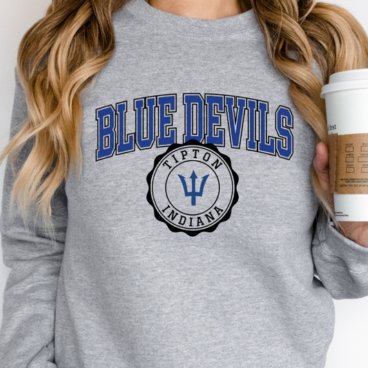Woman holding a coffee cup, wearing a grey crewneck sweatshirt featuring a collegiate-style Tipton Blue Devils and Indiana seal graphic.