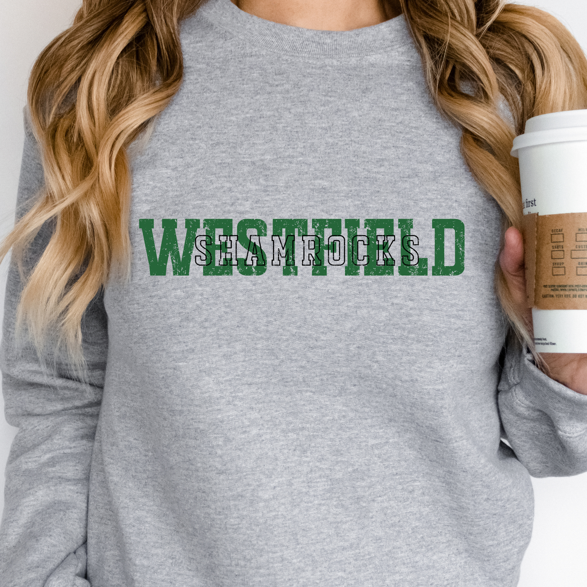 A person wearing a soft grey crewneck sweatshirt featuring "WESTFIELD" in large green block letters with "SHAMROCKS" layered in a black-outlined font across the center.