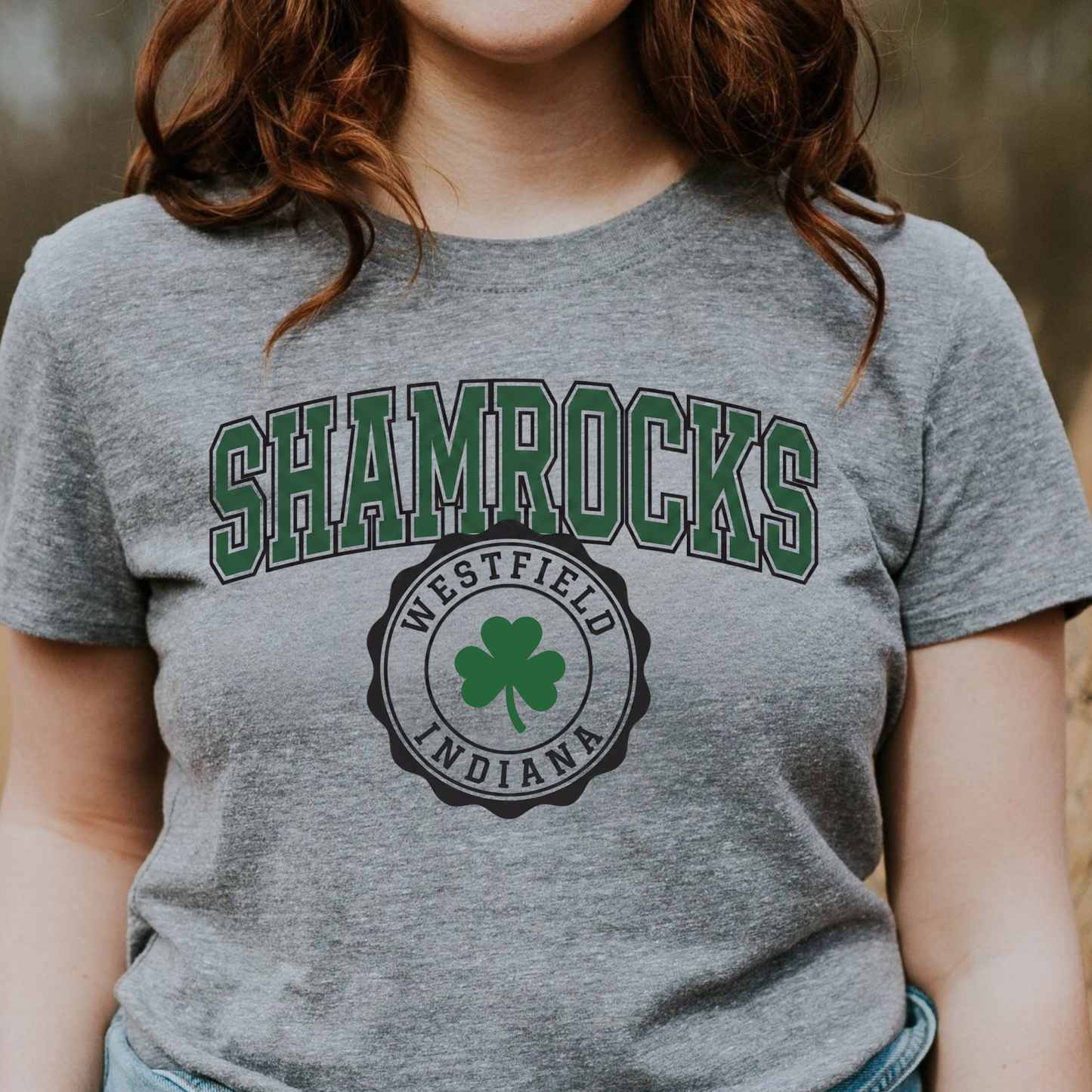 A person wearing a grey t-shirt featuring a collegiate-style 'SHAMROCKS' arch design above a circular 'WESTFIELD INDIANA' shamrock seal.