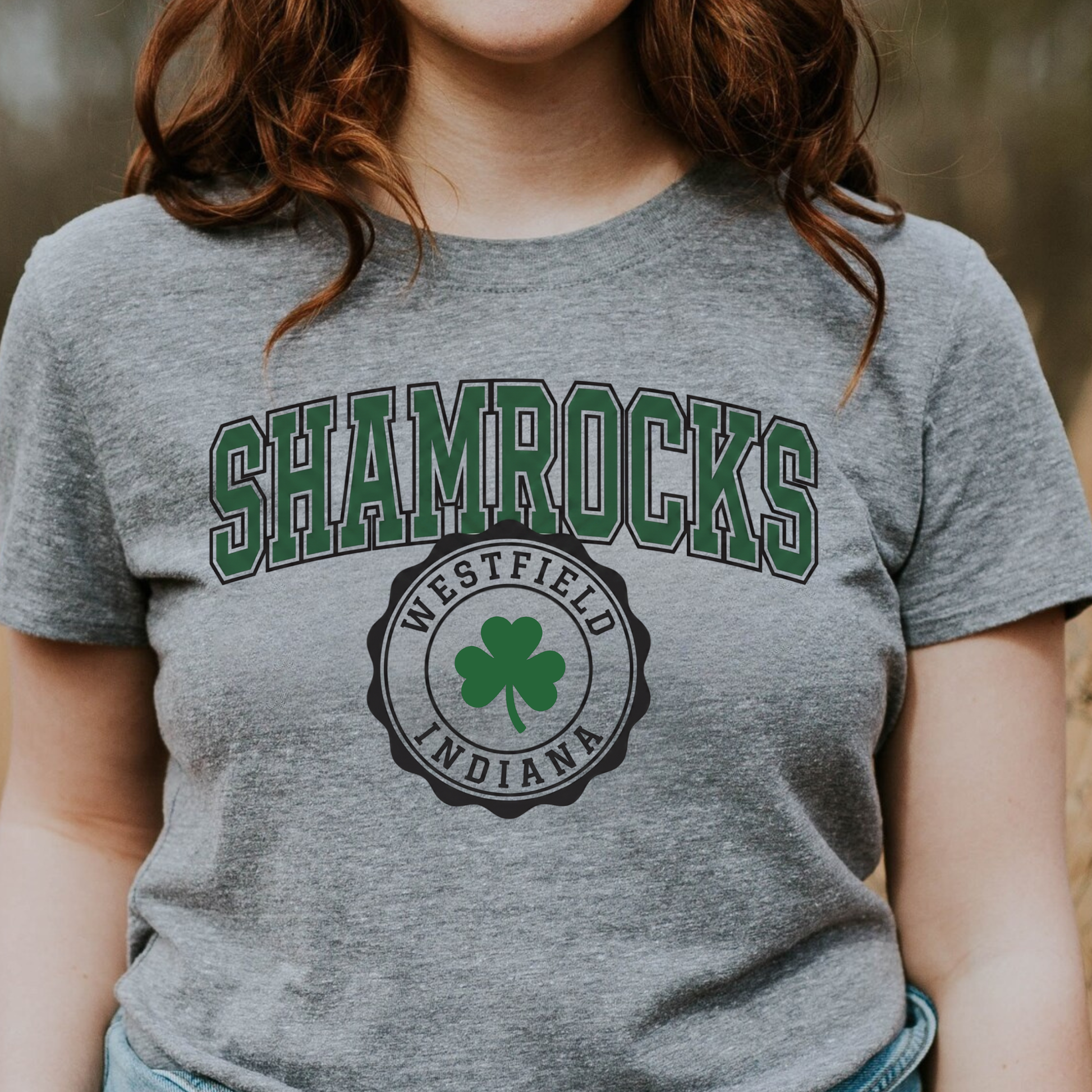 A person wearing a grey t-shirt featuring a collegiate-style 'SHAMROCKS' arch design above a circular 'WESTFIELD INDIANA' shamrock seal.