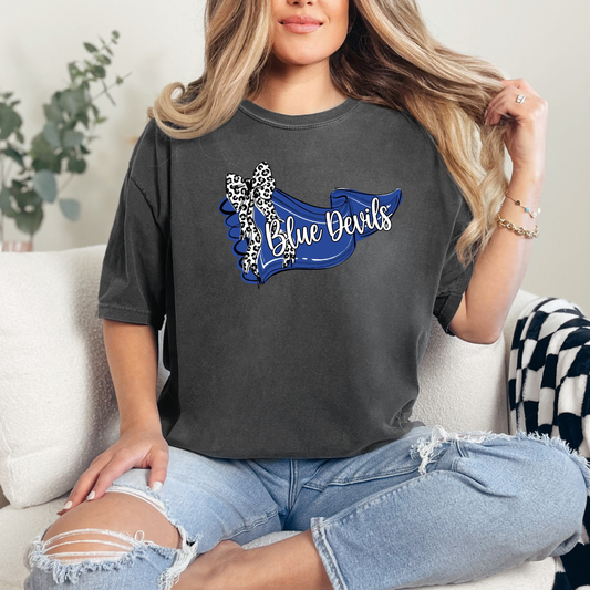 Woman wearing a charcoal graphic t-shirt featuring a blue 'Blue Devils' banner design with a leopard-print bow.