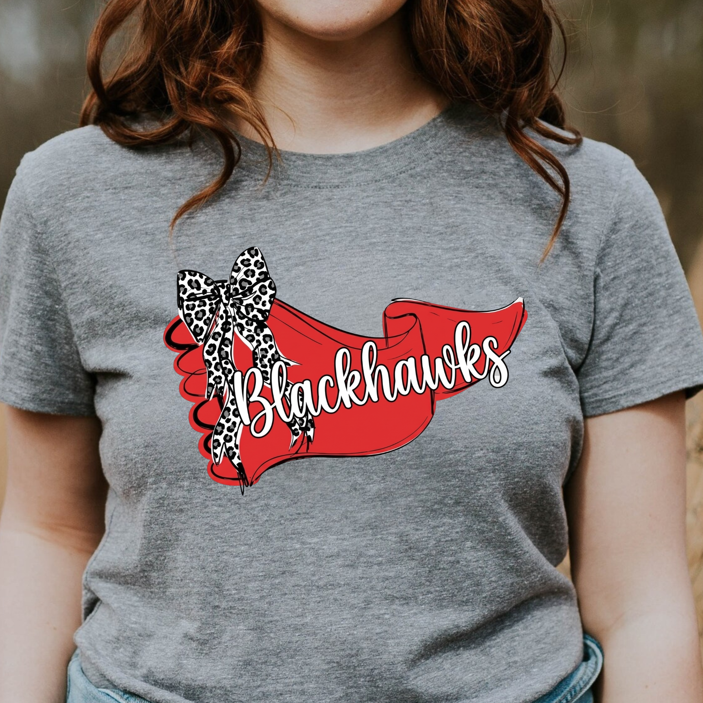 Close-up of a woman in a grey graphic t-shirt showcasing a Blackhawks team banner design with a leopard-print bow.