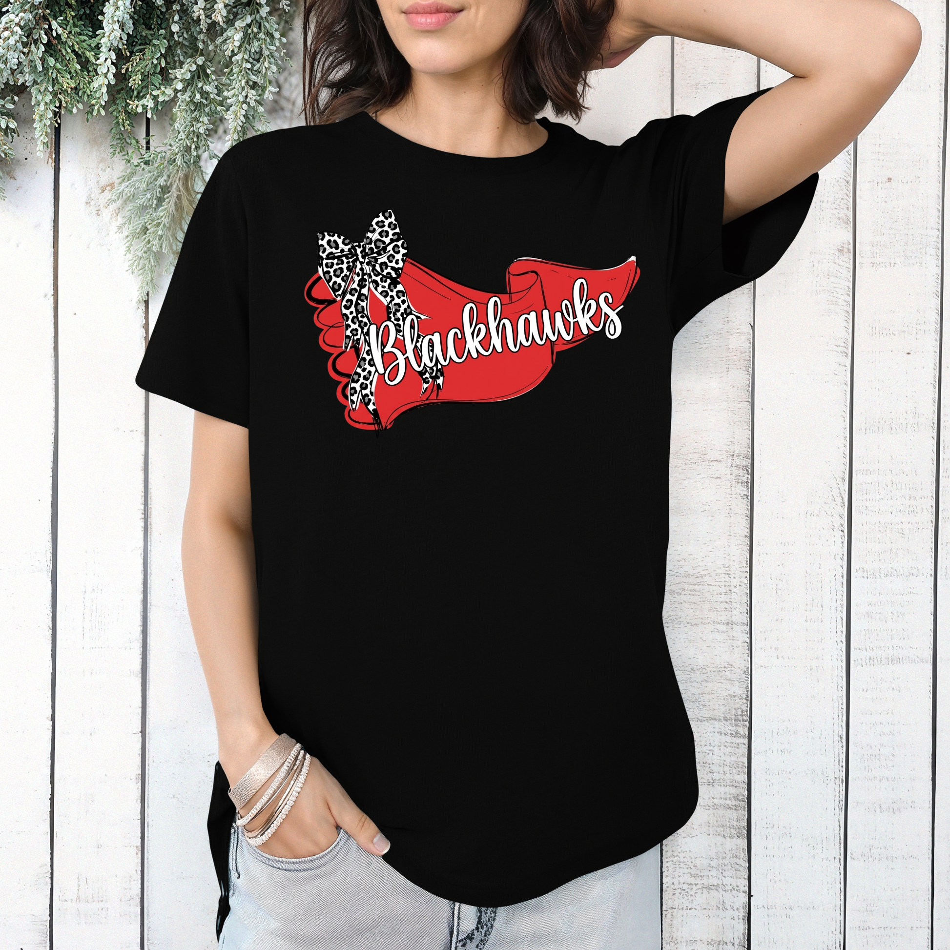 Woman wearing a black graphic t-shirt featuring a Sheridan Blackhawks banner and leopard bow detail, styled in a relaxed, comfortable fit.