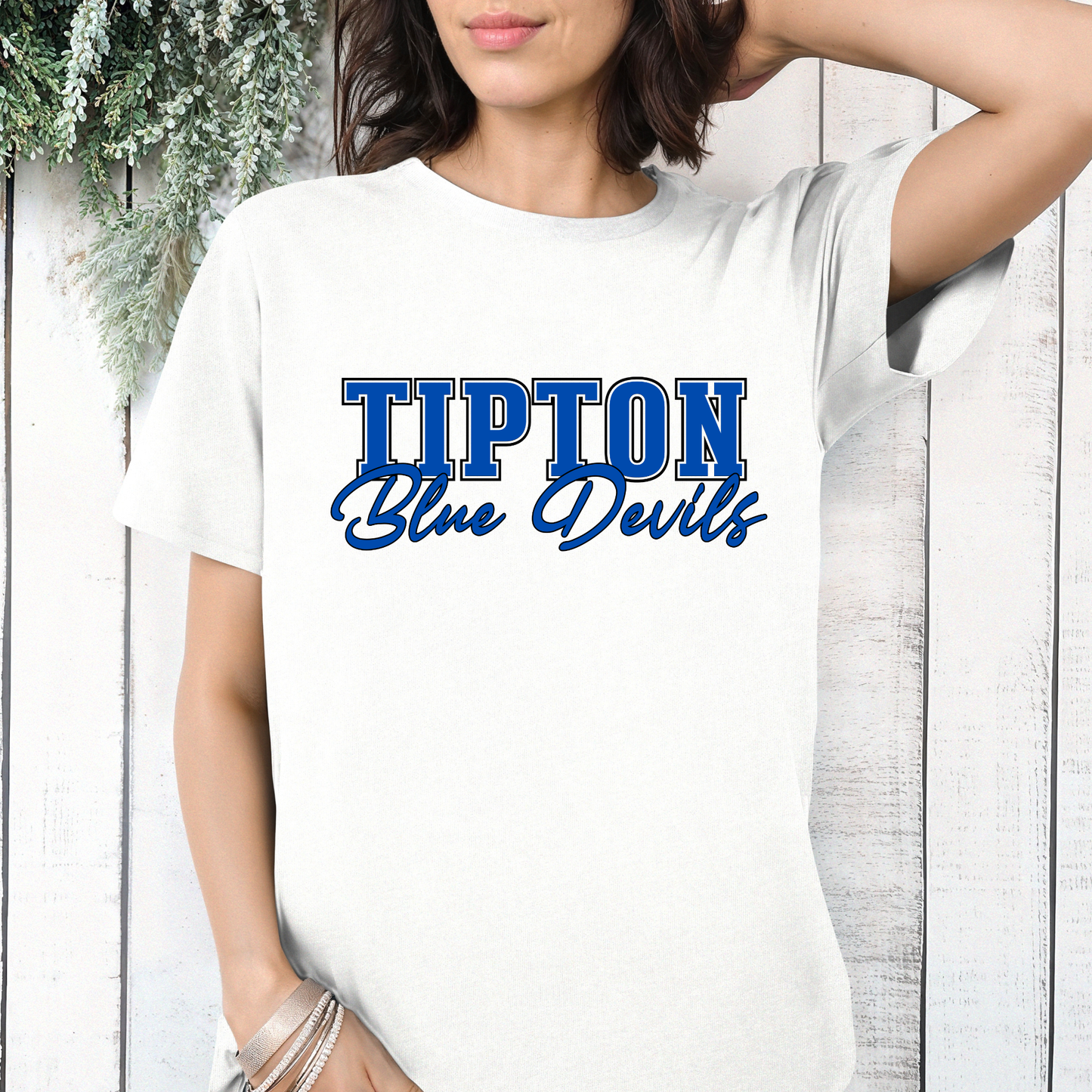 Woman wearing a white Tipton Blue Devils Script Spirit Shirt featuring bold Tipton lettering and Blue Devils script design in royal blue and white school colors.