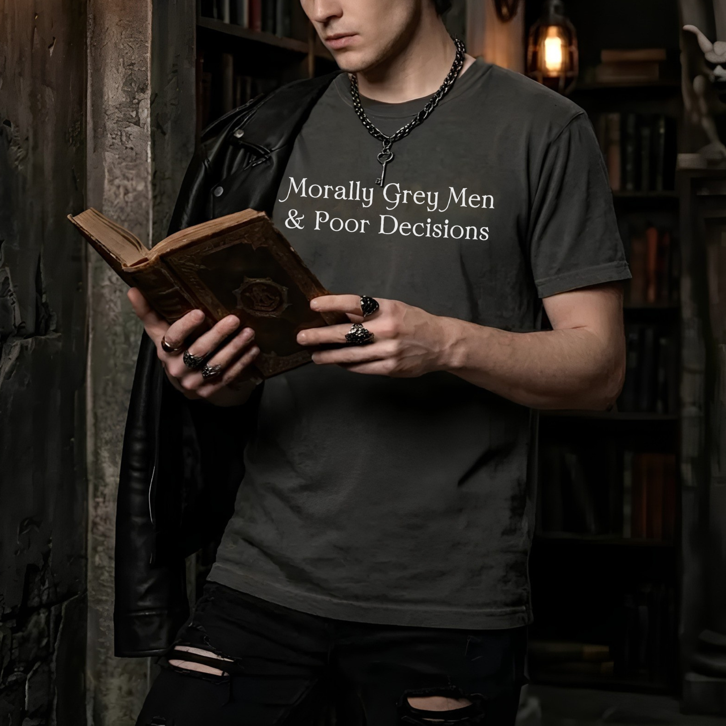 Man wearing Morally Grey Men & Poor Decisions shirt while reading a fantasy book in a dark academia library setting