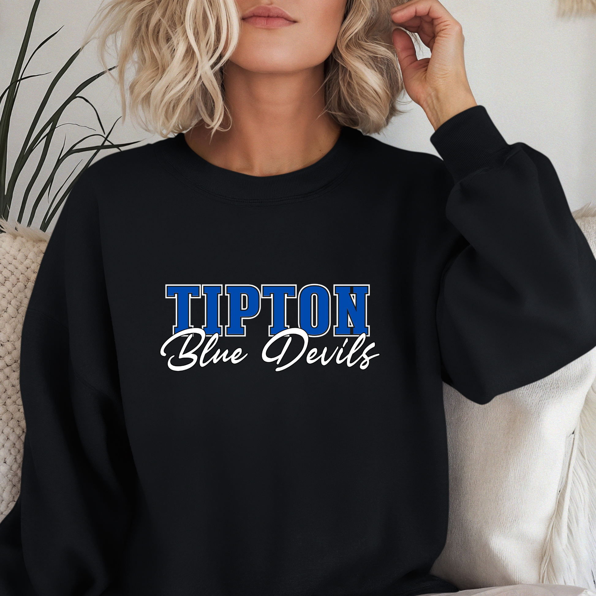 Woman wearing a black Tipton Blue Devils Script Spirit Crewneck Sweatshirt featuring bold blue varsity lettering with Blue Devils script design in royal blue, white, and black school colors.