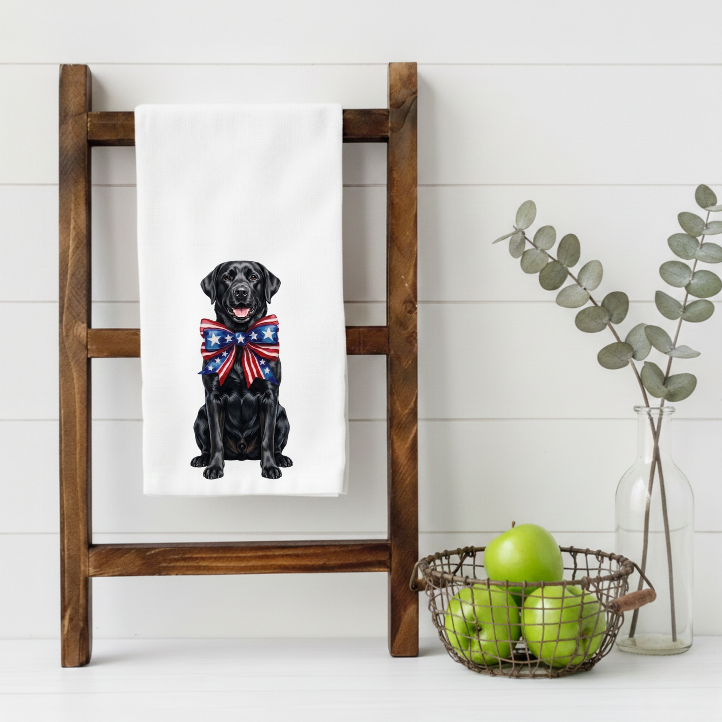 Black dog with a patriotic bow tie on a white towel hanging on a wooden ladder against a white wall.