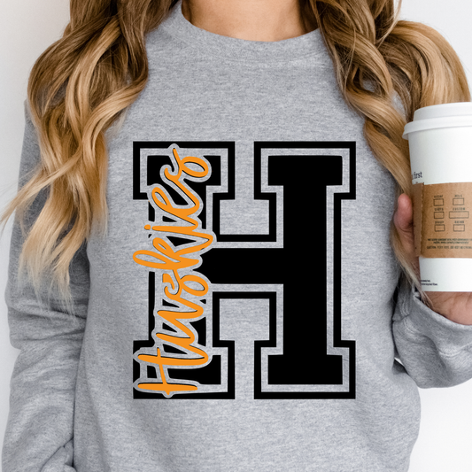 Woman wearing a Hamilton Heights Huskies varsity letter H design with orange Huskies script printed on heather gray Gildan crewneck sweatshirt