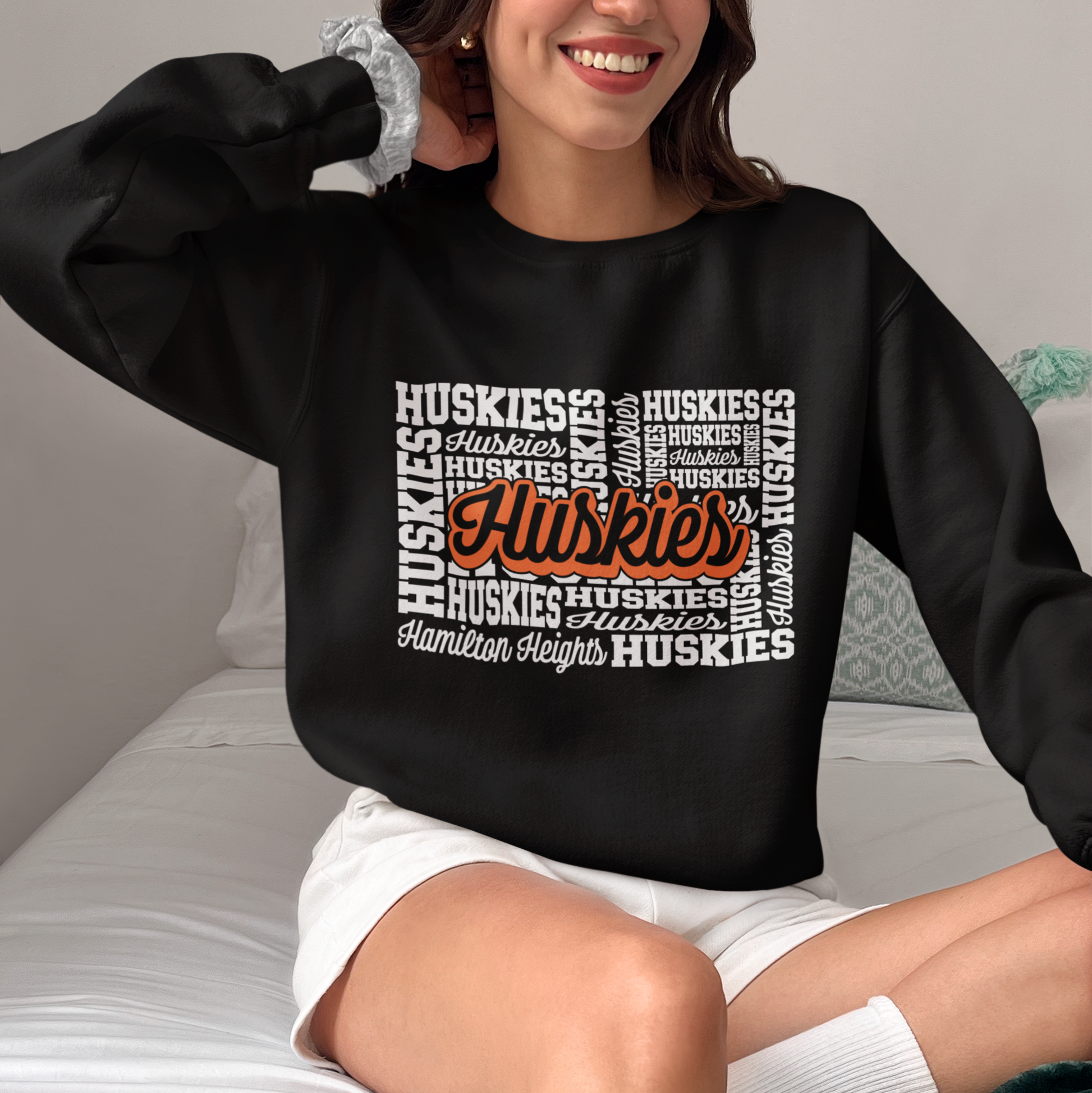 Woman wearing a Hamilton Heights Huskies Word Collage crewneck, black sweatshirt with bold orange and white typography.