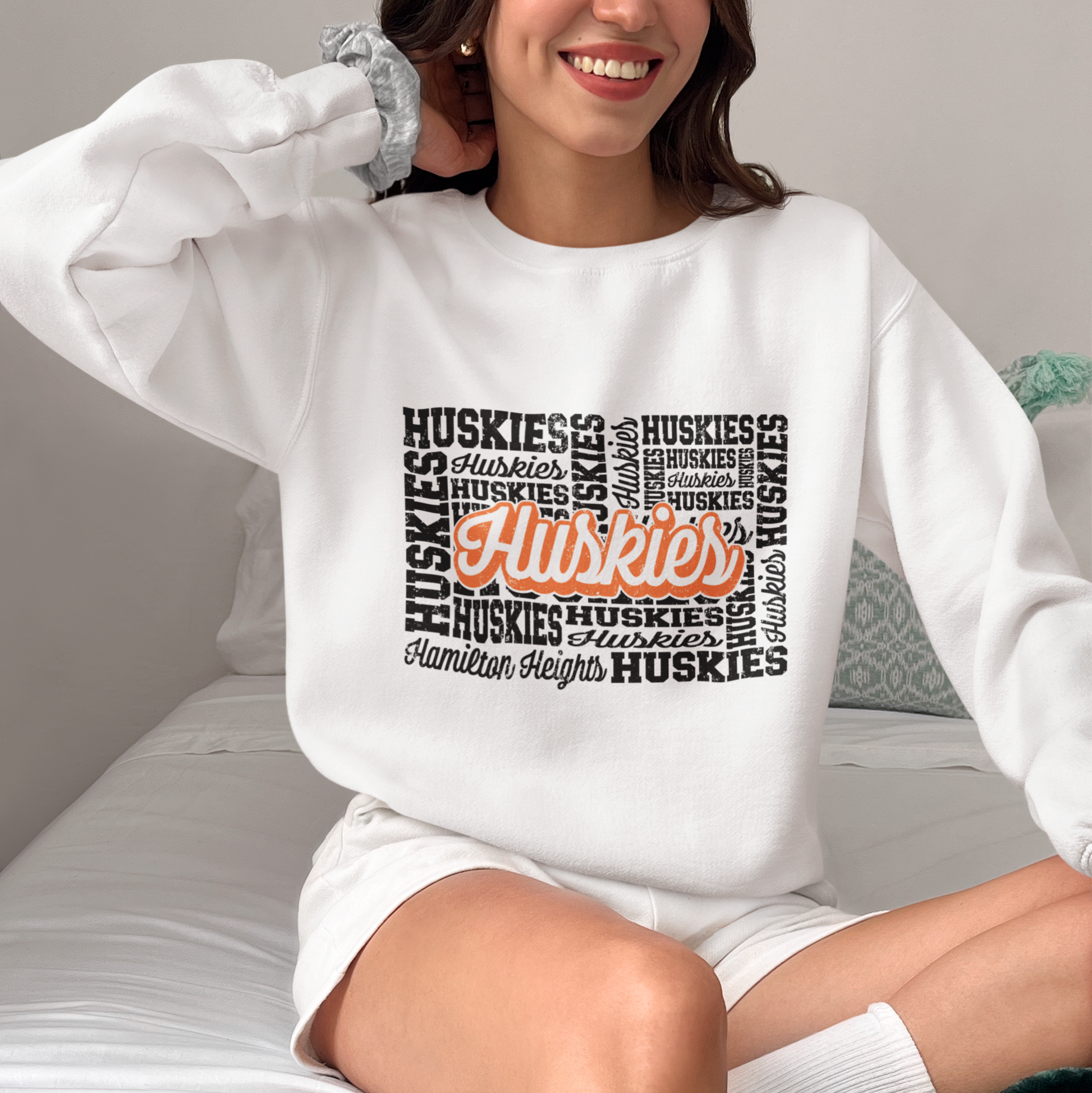 Woman wearing a Hamilton Heights Huskies Word Collage crewneck, black sweatshirt with bold orange and white typography.