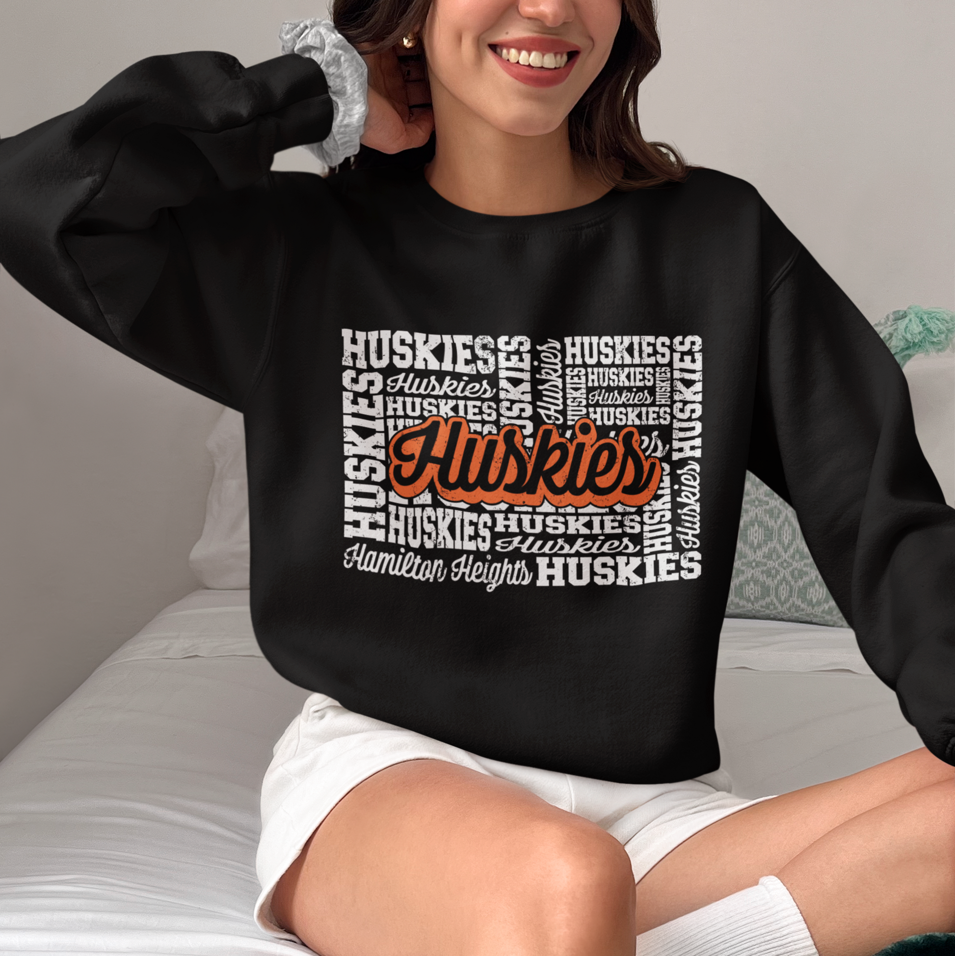 Woman wearing a Hamilton Heights Huskies Word Collage crewneck, black sweatshirt with bold orange and white typography.